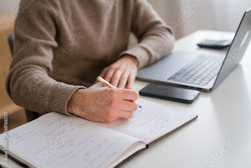 Crop man writing in notepad while working on project