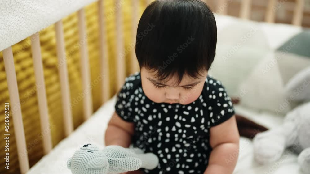 Adorable hispanic baby holding toy sitting on cradle at bedroom Adorable hispanic baby holding toy sitting on cradle at bedroom