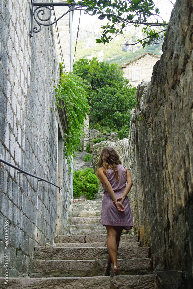 A girl in a short dress climbs the stairs on an old city street with her hands behind her back A girl in a short dress climbs the stairs on an old city street with her hands behind her back