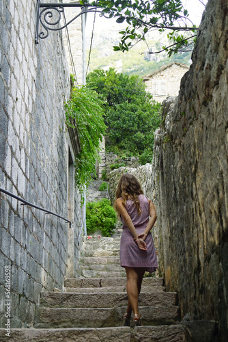 A girl in a short dress climbs the stairs on an old city street with her hands behind her back