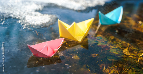 Multicolored paper boats. Colorful pink yellow blue orange ships in big spring snow puddle on winter street. Warm wet rainy weather, old grass. Hello spring, autumn. Children play, have fun outdoors