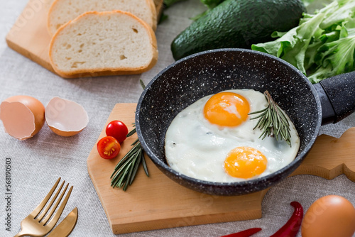 Fried eggs in a frying pan with rosemary, bread, eggs and green salad on a linen tablecloth. Breakfast, lunch and dinner. The view is soft, selective focus. Rustic style.