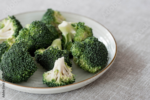 Fresh green broccoli on a plate on a linen tablecloth. Broccoli cabbage leaves. Light background. Vegetarian food. Healthy lifestyle.