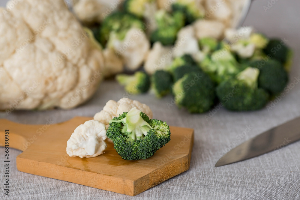 Fresh green broccoli and cauliflower on a wooden chopping board on a linen tablecloth. Broccoli cabbage leaves. Light background. Vegetarian food. Healthy lifestyle.