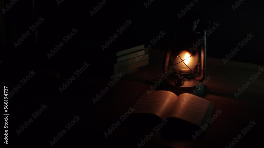 An ancient kerosene lamp, standing on the table, a book next to it, darkness around. Black background, light from a lamp