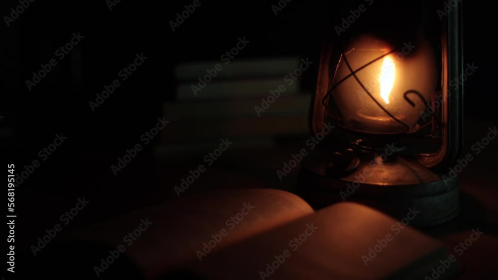 An ancient kerosene lamp, standing on the table, a book next to it, darkness around. Black background, light from a lamp