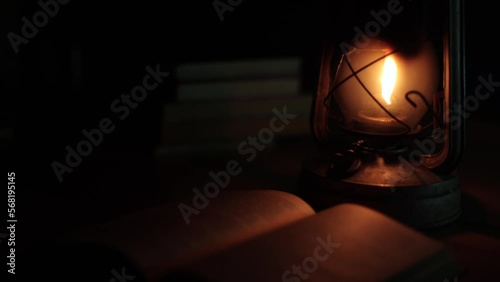 An ancient kerosene lamp, standing on the table, a book next to it, darkness around. Black background, light from a lamp