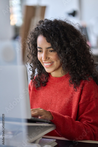 Young happy latin business woman office worker, company employee or student using laptop, typing on computer sitting at desk in office watching online webinar, elearning course looking at pc. Vertical