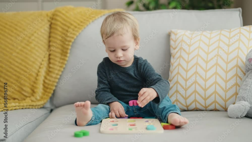 Adorable blond toddler playing with maths game sitting on sofa at home Adorable blond toddler playing with maths game sitting on sofa at home