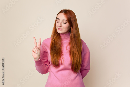 Young red hair woman isolated joyful and carefree showing a peace symbol with fingers.