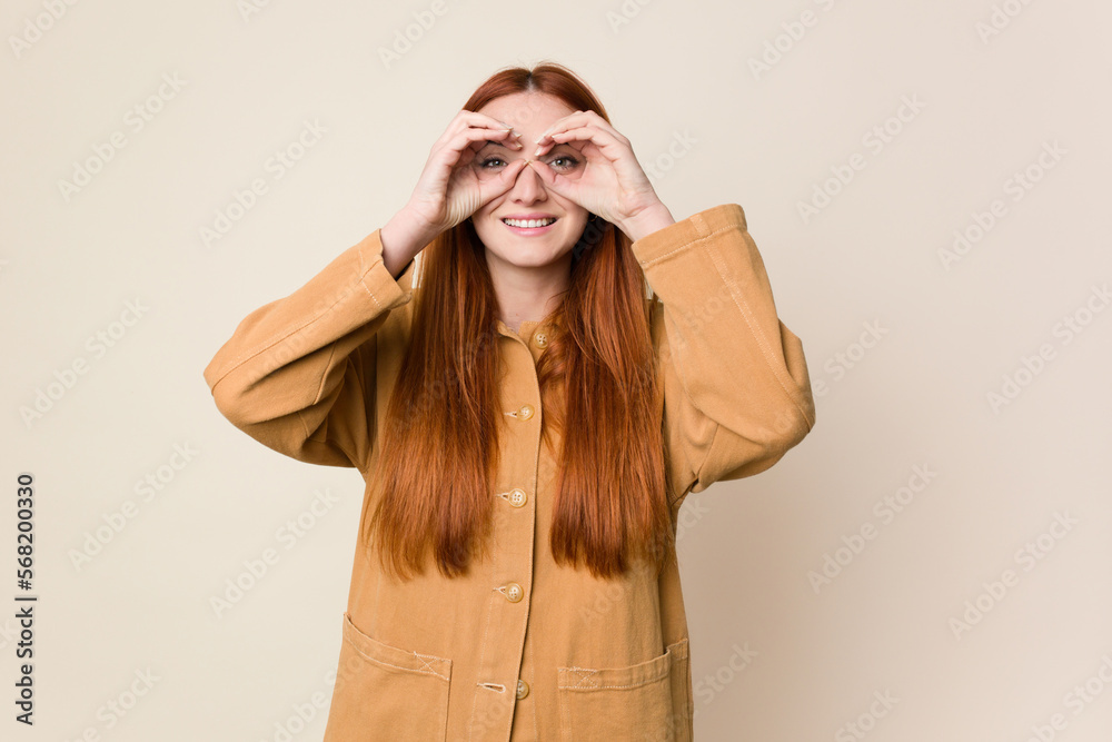 Young red hair woman isolated showing okay sign over eyes Young red hair woman isolated showing okay sign over eyes