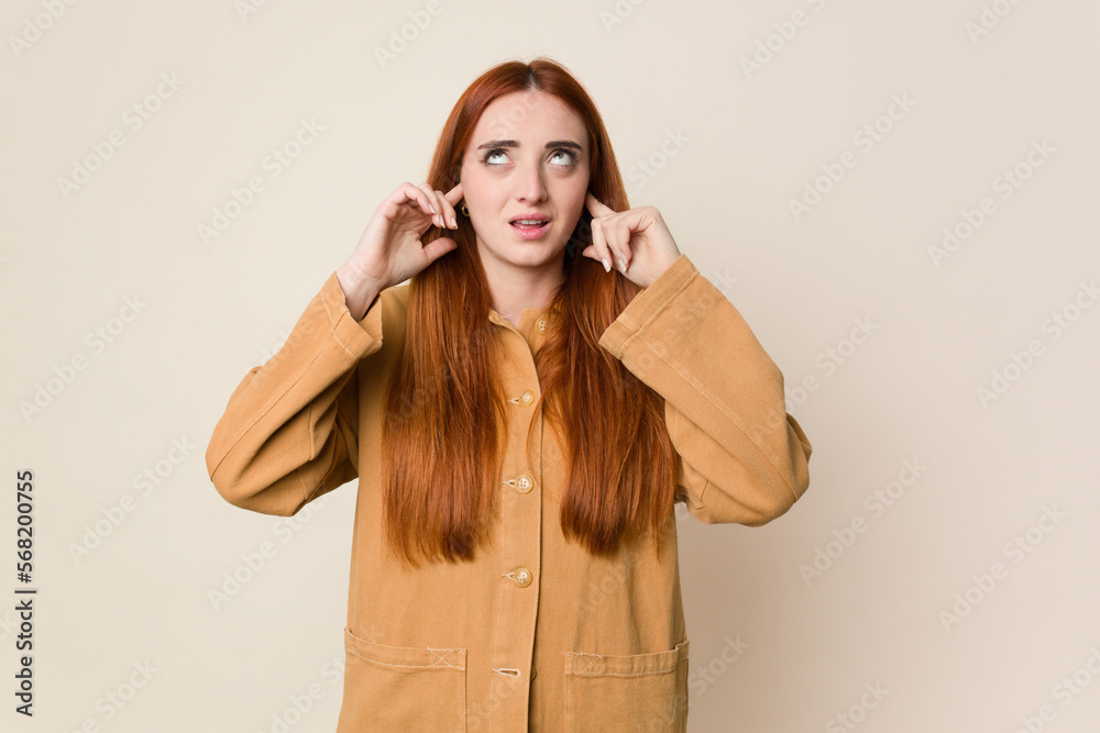 Young red hair woman isolated covering ears with fingers, stressed and desperate by a loudly ambient. Young red hair woman isolated covering ears with fingers, stressed and desperate by a loudly ambient.