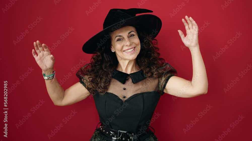 Middle age hispanic woman wearing witch costume having halloween party over isolated red background Middle age hispanic woman wearing witch costume having halloween party over isolated red background