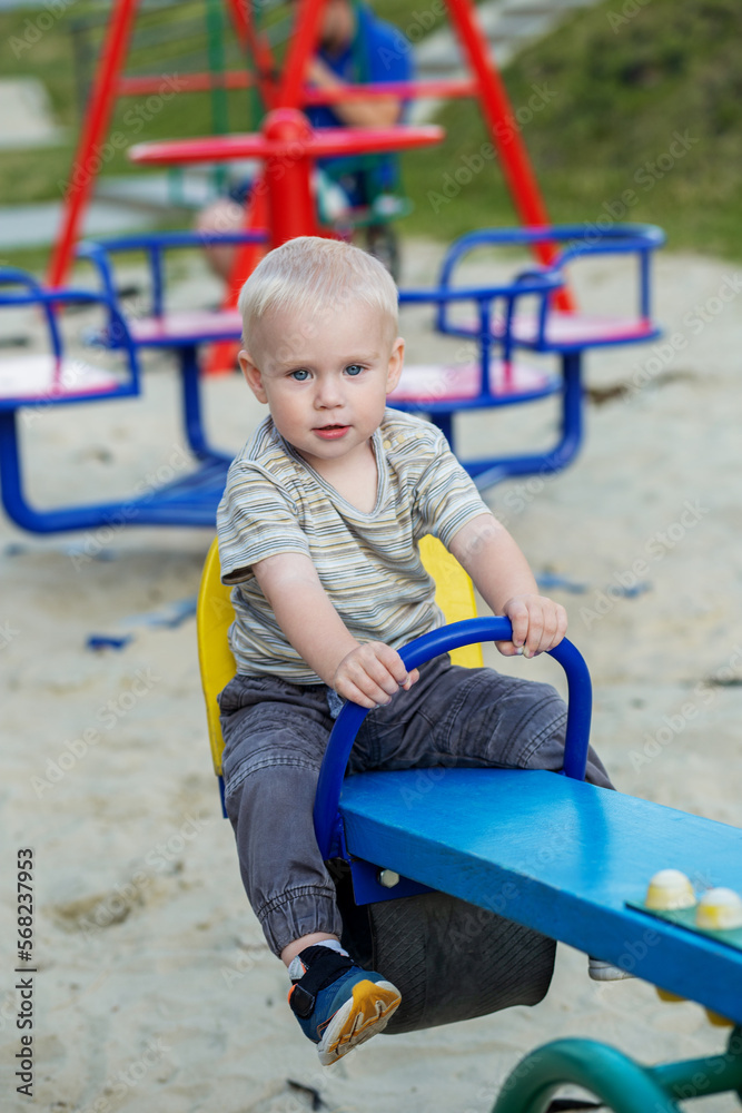 Cute kid having fun on seesaw at playground. Concept of kindergarten. Vertical Cute kid having fun on seesaw at playground. Concept of kindergarten. Vertical