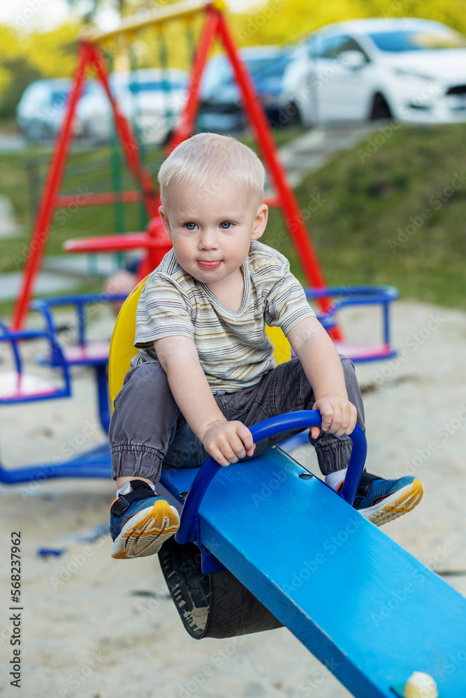 Cute kid having fun on seesaw at playground. Concept of kindergarten. Vertical Cute kid having fun on seesaw at playground. Concept of kindergarten. Vertical