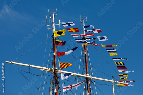 International maritime signal flags on a flagpole and masts on a sailing ship with a blue sky in the background.