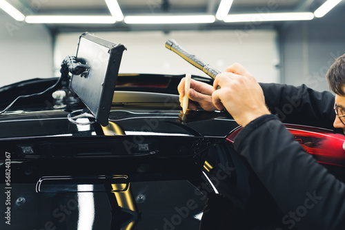Man removing dent on black car trunk lid. Professional Paintless Dent Repair. Indoor closeup shot. Mechanic and car detailing studio. High quality photo photo