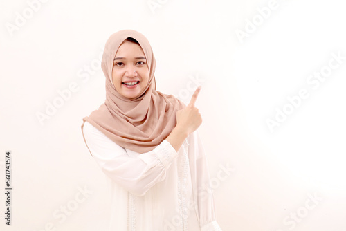 Happy young asian muslim woman standing while pointing at empty space. Isolated on white © pakWw