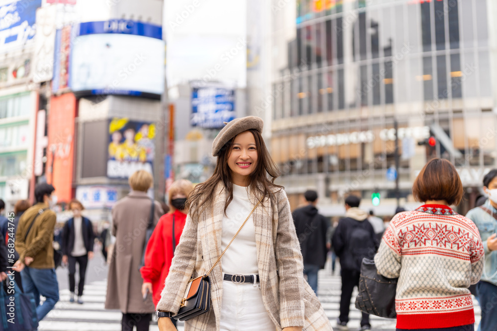 Happy Asian woman shopping and crossing street crosswalk with crowd of people at Shibuya, Tokyo, Japan in autumn. Attractive girl  enjoy and fun outdoor lifestyle travel in city on holiday vacation.