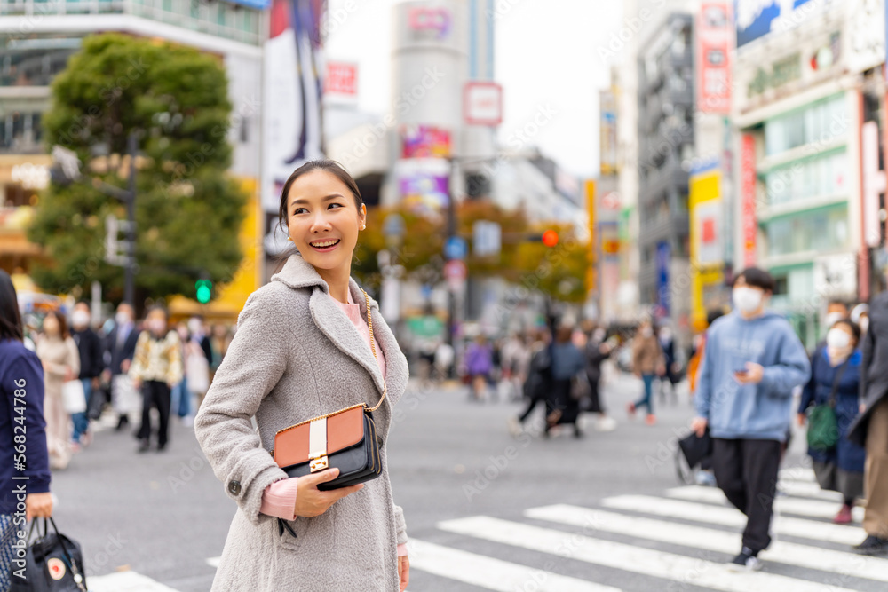 Happy Asian woman shopping and crossing street crosswalk with crowd of people at Shibuya, Tokyo, Japan in autumn. Attractive girl  enjoy and fun outdoor lifestyle travel in city on holiday vacation.