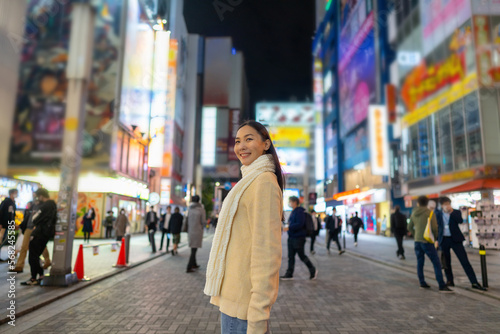 Asian woman shopping and crossing street crosswalk with crowd of people at Shibuya, Tokyo, Japan at night. Attractive girl enjoy and fun outdoor lifestyle travel in city on autumn holiday vacation.