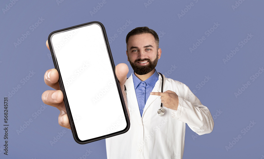 Smiling Male Doctor Pointing At Big Blank Smartphone In His Hand Smiling Male Doctor Pointing At Big Blank Smartphone In His Hand