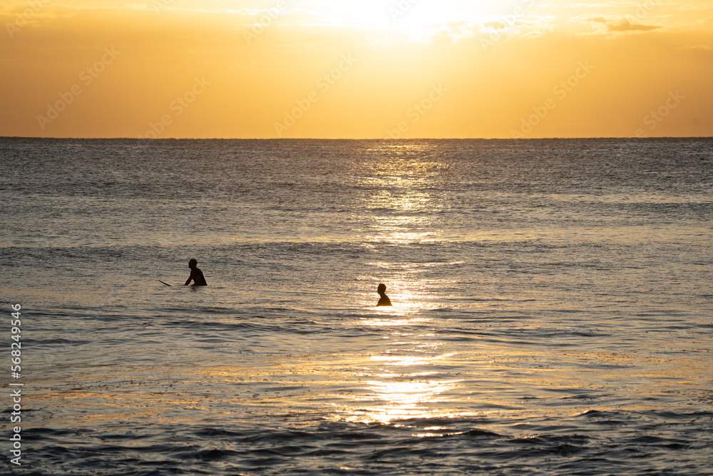 Silhouette of two surfers in the ocean at sunrise
