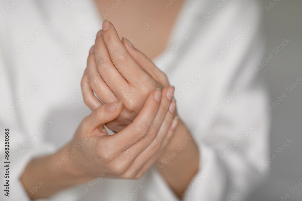 Young european female in white silk robe applies cream on hands, enjoys daily procedures in bedroom, close up