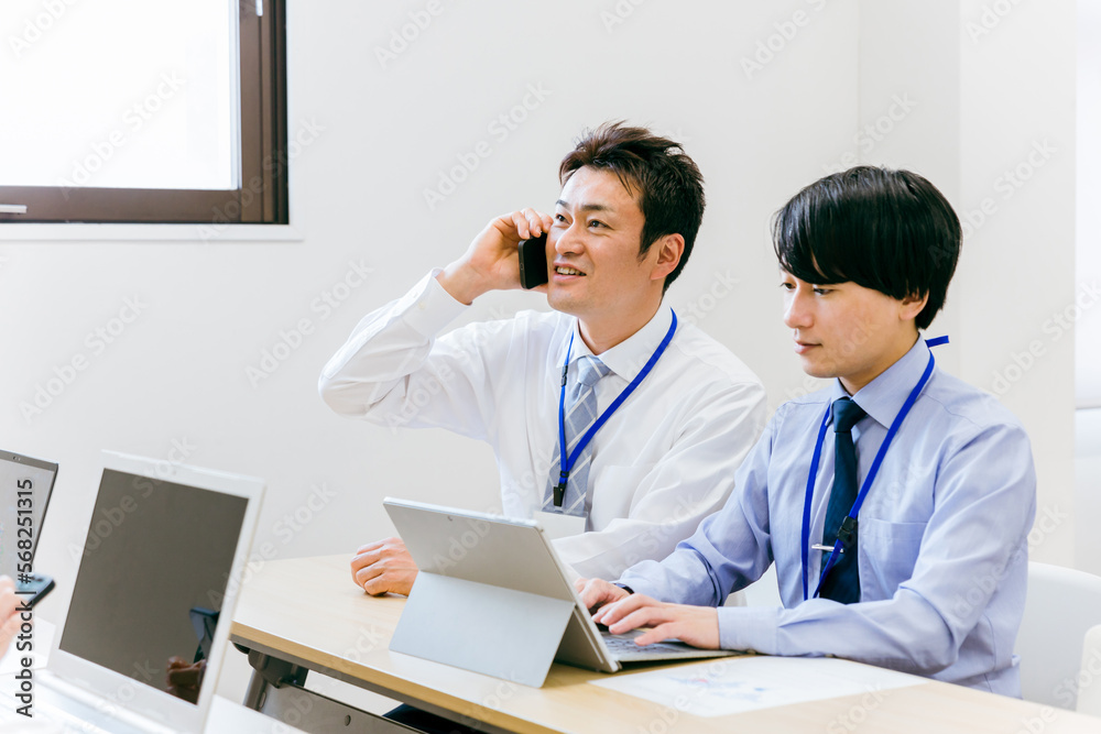 会社のオフィス・会議室で電話する上司と冷静に仕事するビジネスマン(アジア人・日本人・中国人) 会社のオフィス・会議室で電話する上司と冷静に仕事するビジネスマン(アジア人・日本人・中国人)