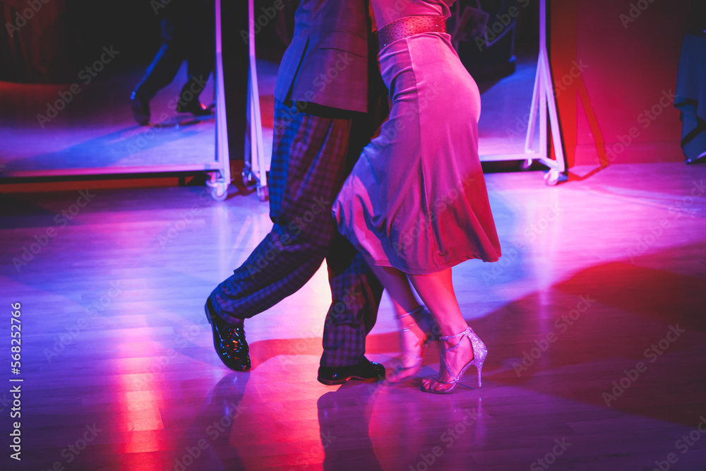 Fototapeta premium Couples dancing traditional latin argentinian dance milonga in the ballroom on a festival, tango studio, salsa, bachata and kizomba lesson in the red and purple lights, rehearsal in the dance class