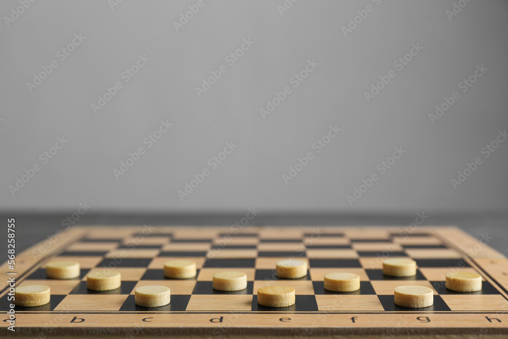 Wooden checkerboard with game pieces on light grey background, closeup. Space for text Wooden checkerboard with game pieces on light grey background, closeup. Space for text