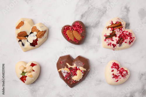 Tasty chocolate heart shaped candies with nuts on white marble table, flat lay