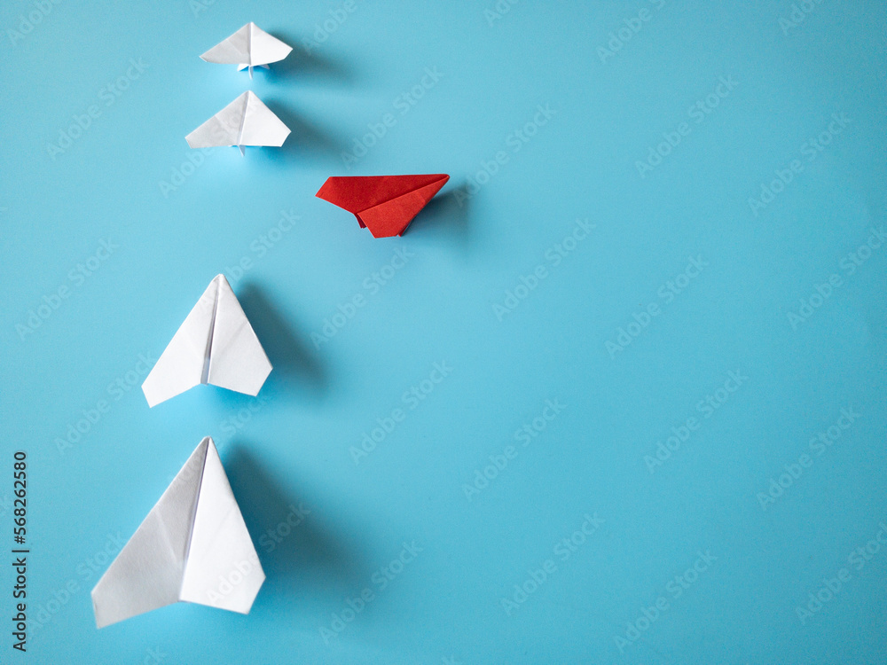 Red paper plane origami leaving other white planes on blue background. Copy space and leadership skills concept. Red paper plane origami leaving other white planes on blue background. Copy space and leadership skills concept.