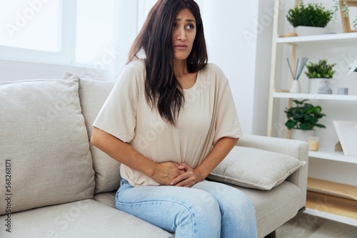 Woman sitting on sofa at home back and stomach pain during menstruation, women's day, women's health problems, suspected appendicitis