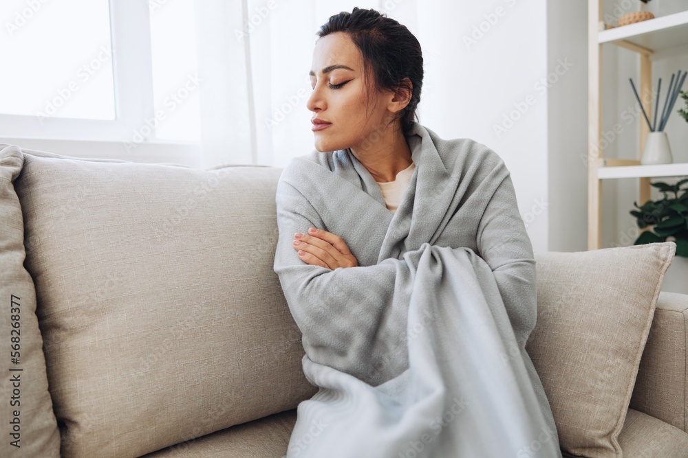 Woman cold headache runny nose and stuffy nose sitting on sofa in plaid, treatment for flu, allergies and covid-19 Woman cold headache runny nose and stuffy nose sitting on sofa in plaid, treatment for flu, allergies and covid-19