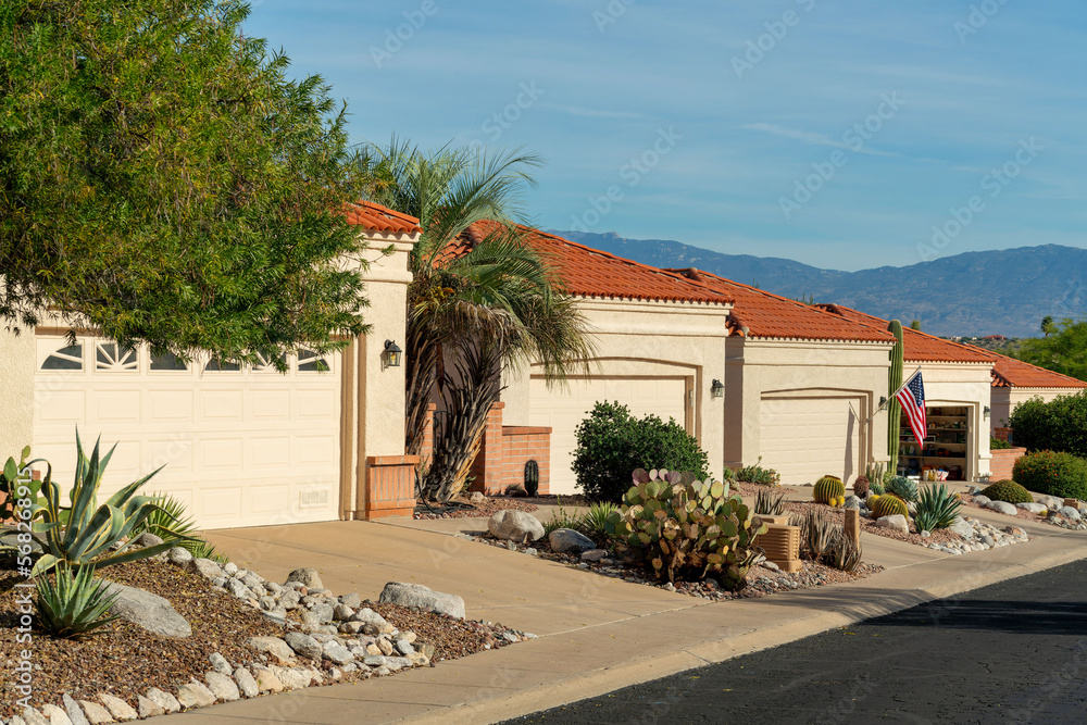 Row of modern adobe style one story houses in desert community of arizona with visible garage doors and front yards