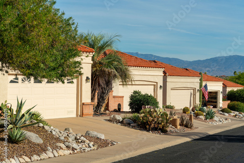 Row of modern adobe style one story houses in desert community of arizona with visible garage doors and front yards © Aaron