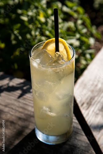 Tom Collins cocktail sitting in the sun on patio bar with lemon wheel garnish