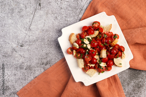 Tomato and mozzarella salad with herbs and croutons on a white square  plate on a dark background. Top view, flat lay
