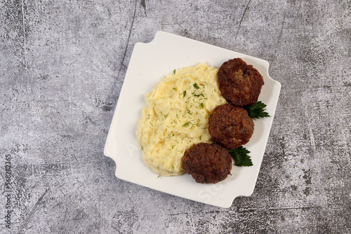 Mashed potatoes with cutlets and herbs on a white square  plate on a dark background. Top view, flat lay