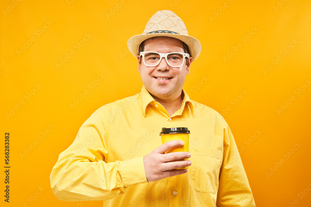 Energetic funny man holding and drinking cup of takeaway coffee, smiling and enjoying drink isolated on yellow background Energetic funny man holding and drinking cup of takeaway coffee, smiling and enjoying drink isolated on yellow background