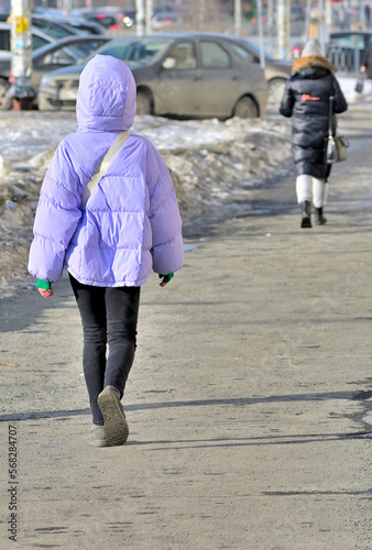 A young woman walks along the sidewalk on a winter day