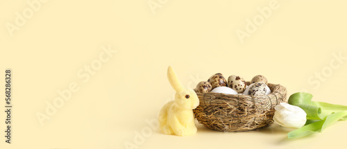 Fototapeta Naklejka Na Ścianę i Meble -  Nest with Easter eggs, bunny and tulip flower on light yellow background with space for text