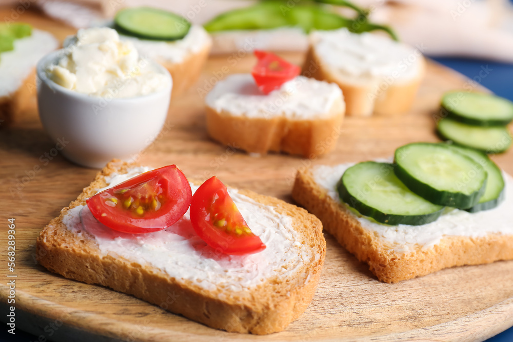 Wooden board of tasty sandwiches with cream cheese and vegetables, closeup