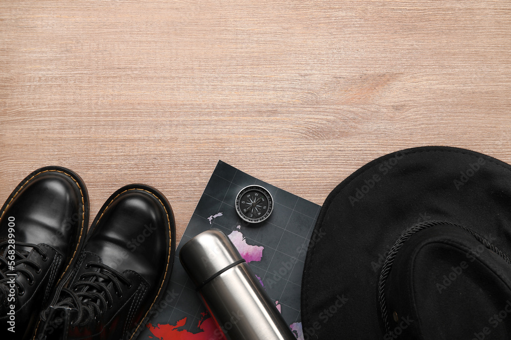 Compass with thermos, map, hat and boots on wooden background Compass with thermos, map, hat and boots on wooden background