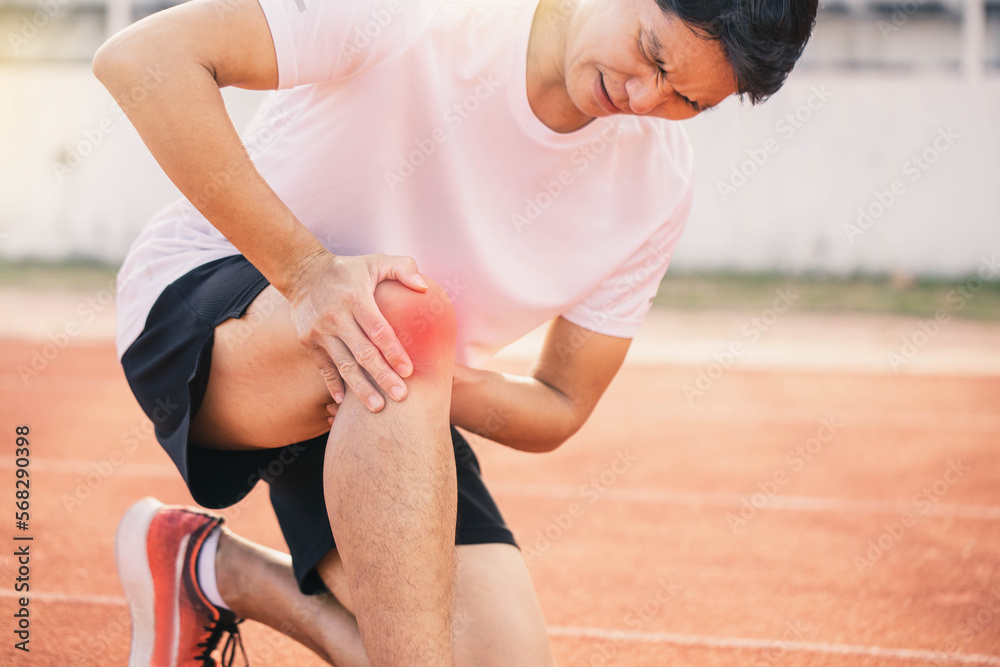 Injured by fitness concept. Man using hands on his knees while working on the street in a park with copy space for text. runner have knee ache due to Runners Knee .