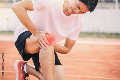 Injured by fitness concept. Man using hands on his knees while working on the street in a park with copy space for text. runner have knee ache due to Runners Knee .