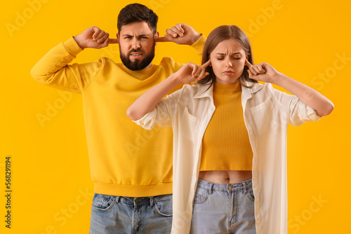 Принти на полотні Young couple suffering from loud noise on yellow background