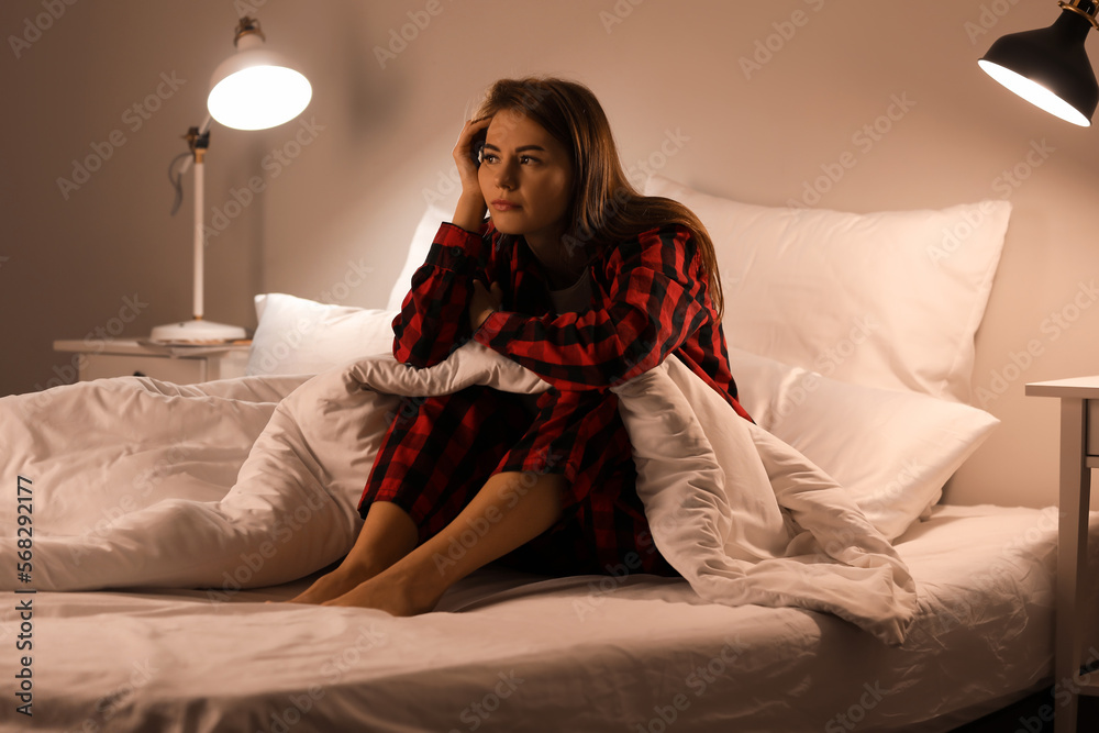 Obraz premium Upset young woman sitting on bed at night