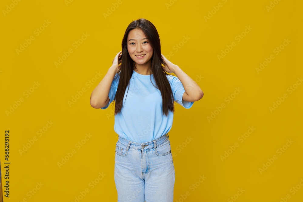 Asian woman smile with teeth hand gestures, signs and symbols on yellow background in blue t-shirt and jeans Asian woman smile with teeth hand gestures, signs and symbols on yellow background in blue t-shirt and jeans